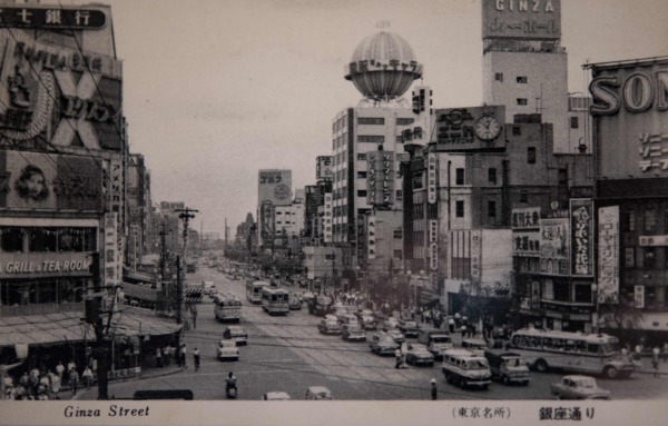 【34】商人の気質、銀座らしさを継承。高度経済成長期の銀座。60年代、70年代の高度経済成長期になると、関西など全国から、銀座にやってきて商売をする人々が増えた。銀座の商売人が自ら店頭に立って丁寧に接客するのとは異なり、大阪の商売人は品揃えや安く提供することに専念し、販売は若い店員に任せ、店主は仕入れに徹する。昔から銀座で商売をしている旦那衆にしてみれば、銀座らしさが失われると心配した。結局、地方から銀座にやってきた人々が、銀座のスタイルに自ら同化（銀座ナイズ）していくことになる。「今までのやり方では商売にならない。売るためには銀座の流儀を守らなくては」と考えた。今でも銀座には関西出身の商店主が多く、銀座らしさが継承されているのである。【34】1962(昭和37年)頃・（東京名所）銀座通り