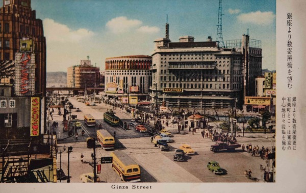 【23】二・二六事件の舞台にもなったモダニズム建築の傑作。今はなき有楽町の日劇と朝日新聞本社。朝日新聞は、1888年(明治21年)大阪にあった朝日新聞社が自由燈、燈新聞の流れを汲む新聞を買収し、東京朝日新聞と名前を変え創刊したのがルーツである。当時の社屋は、現在の銀座6丁目(旧・京橋区瀧山町)にあった。1907年(明治40年)夏目漱石が小説記者として、1909年(明治42年)石川啄木が校正係として入社したという驚きの社歴を持つ。1927年(昭和2年)有楽町の新社屋に移転。モダニズム建築の代表作として建築史上知られる白木屋デパートを手掛けた石本喜久治が設計を担当。本社事務機能、印刷工場、読者が来訪できる展示場、大講堂などを備えた多機能ビルだった。5角形の敷地形状に対する配置、階層の動線処理など平面計画に特徴がある。外観は隅角部に丸みを持たせ、事務所窓を端正な矩形、大講堂窓を半楕円形とし、バルコニーを壁面から張り出しアクセントとした。真横を江戸城外掘が流れていた。竣工した年、二・二六事件の舞台となり反乱部隊の襲撃を受ける。1940年(昭和15年)「朝日新聞」に改題。1980年(昭和55年)築地に移転し、跡地が有楽町マリオンとしてなり今に至る。【23】1937年(昭和12年)頃・銀座より数寄屋橋を望む