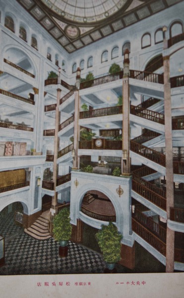 【11】新商法で競い合った百貨店。1872年(明治5年)横浜と新橋をつなぐ日本初の鉄道ができたことで、銀座には、舶来品を扱う商人が、時計商、西洋家具店、洋服店、洋食屋、パン屋などを出店。新進気鋭の商人は、江戸時代からの座売ではなく、ショーウィンドウを設けた。高級商店、専門店な立ち並び、「銀ぶら」という街歩きができる街となる。1924年(大正13年)松坂屋を皮切りに、松屋、三越が進出し東京随一の商業地に。百貨店は、慣例だった下足預かりの廃止し、バス送迎、くじ景品、ヒョウやライオン動物園など、新商法で話題をさらう。この絵葉書は、松屋に現存する中央ホール吹き抜け空間を描いたもの。7フロアを貫き天井高25m。1956年(昭和31)には、東洋一の空中エスカレーター『スカイリボン』が完成し人気を博す。半世紀以上続く名物催事『百傘会』は、数百本の傘が花開く眺めは壮観。娯楽文化を生む松屋を、永井荷風は『断腸亭日乗』の中で「松屋百貨店店飾りの活人形を観るものの如し」と記し、百貨店は大衆化する。【11】1924年(大正13年)・東京銀座 松屋呉服店